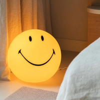 Smiley Bol Lamp ingeschakeld in donkere slaapkamer naast bed met warme gele gloed