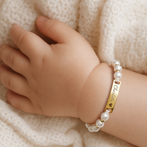 Gepersonaliseerde parelarmband om het polsje van een baby, met de naam Charlotte en een hartje in de goudkleurige naamplaat