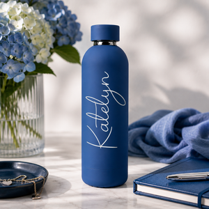 Blauwe RVS drinkfles met gegraveerde naam bij het zwembad met handdoek en zonnebril