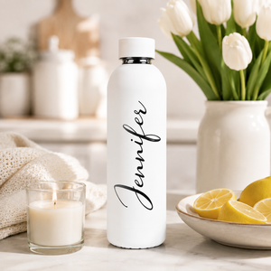 Witte RVS drinkfles met gegraveerde naam naast witte tulpen en een kaars