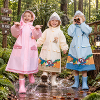 Drie kinderen in roze, beige en lichtblauwe RainBuddy regenjas spelen in de regen in het bos