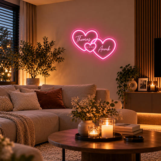 LoveGlow neon dubbel hart in roze met twee namen en een datum, boven de bank in een sfeervolle woonkamer