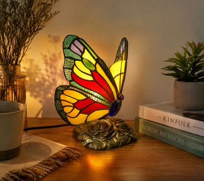 Tiffany vlinderlamp brandend op een houten kastje, glas-in-lood vleugels in rood, geel en groen