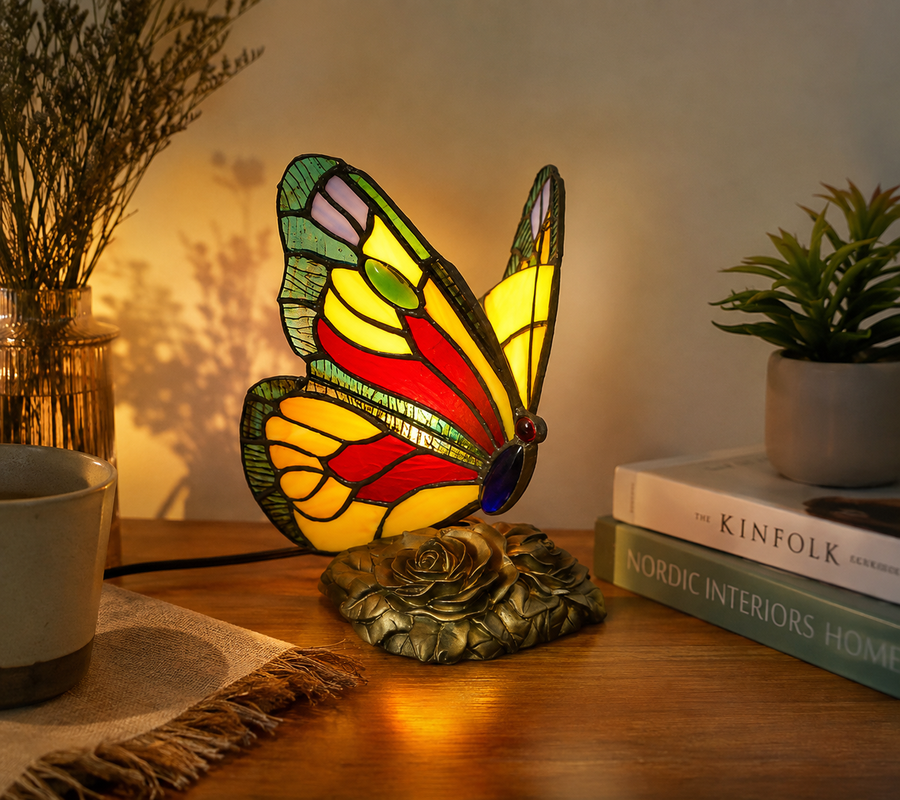Tiffany vlinderlamp brandend op een houten kastje, glas-in-lood vleugels in rood, geel en groen